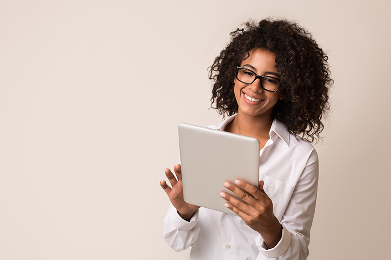 Mulher sorridente, usando óculos e jaleco branco, interagindo com um tablet em um ambiente claro e profissional.